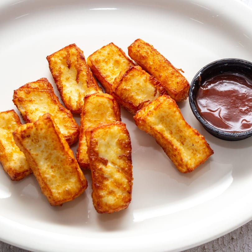 Golden-brown fried cheese sticks, known as sorullitos, with a side of dipping sauce on a white plate.