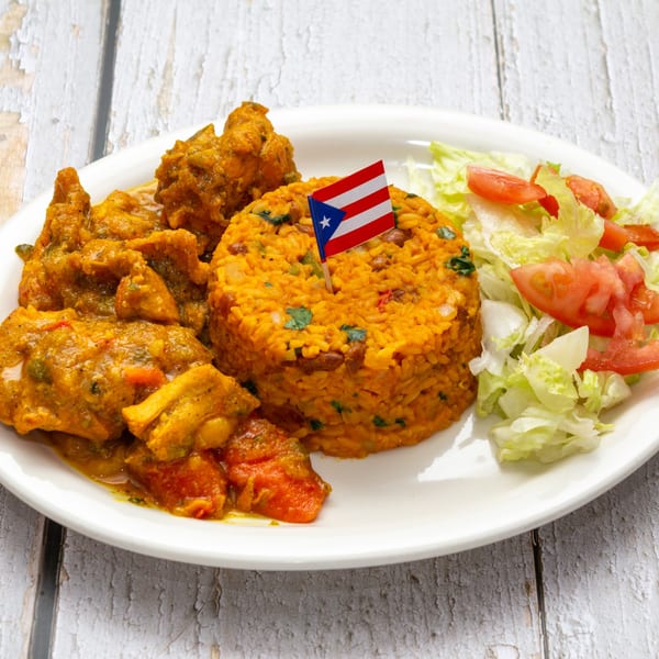 Puerto Rican chicken stew with yellow rice and a side salad on a white plate.
