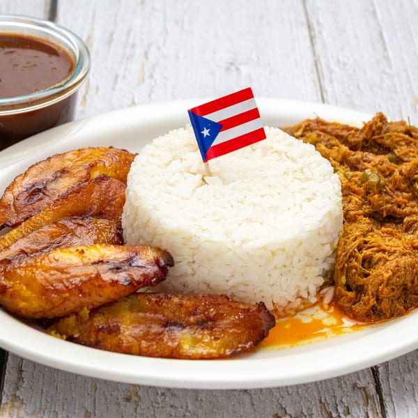 Puerto Rican dish with white rice, shredded meat, fried plantains, and a small Puerto Rican flag.