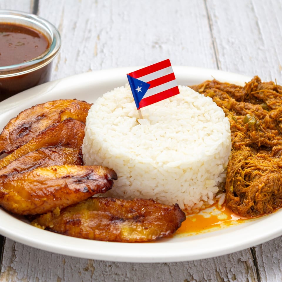 Puerto Rican dish with white rice, shredded meat, fried plantains, and a small Puerto Rican flag.