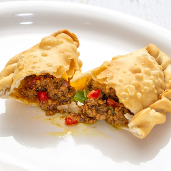 A Puerto Rican empanada, split open to reveal a savory filling of ground meat and vegetables.