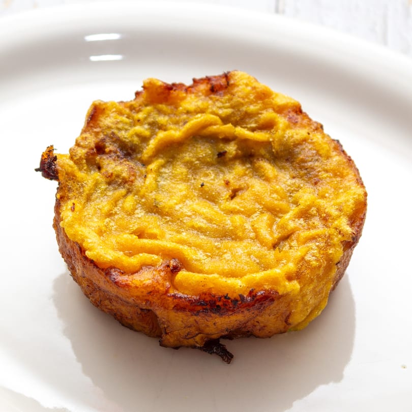 Close-up of a golden-brown, round Puerto Rican alcapurria on a white plate.