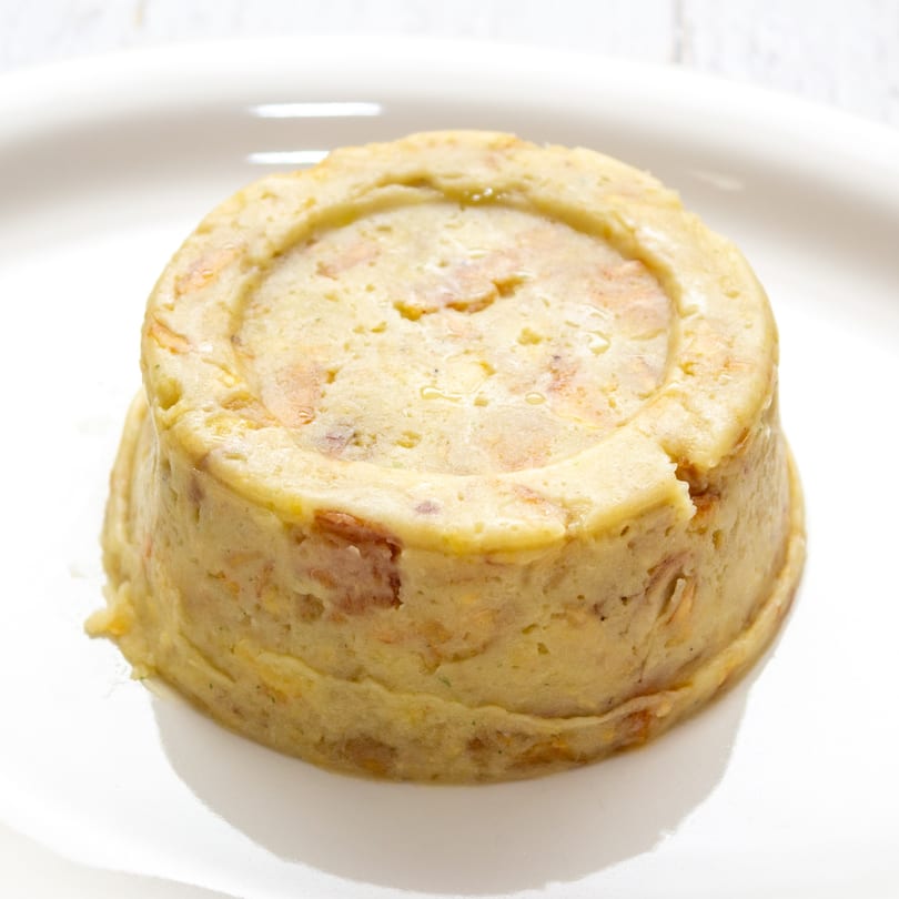 A close-up of a golden-brown Puerto Rican mofongo, a savory plantain dish, on a white plate.